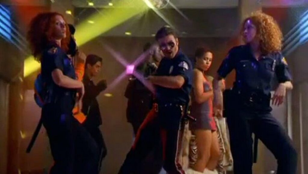 George Michael bailando con dos policías femeninas durante el videoclip de "Outside"
