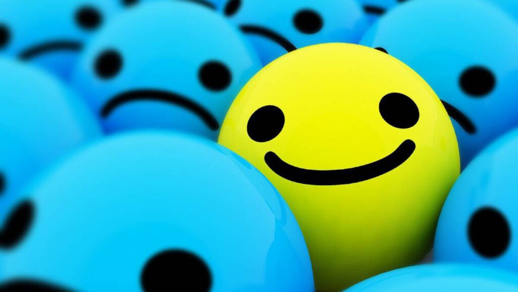 Pelota amarilla con cara sonriente entre pelotas azules con cara triste